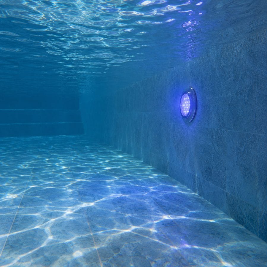 Foco LED RGB encendido en una pared de piscina a profundidad realista